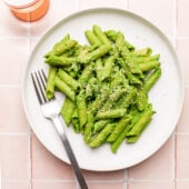 green pasta on white plate with fork and glass