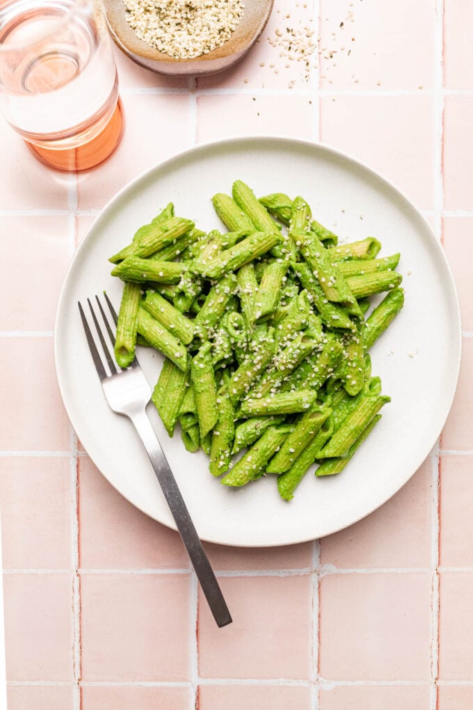 green pasta on white plate with fork and glass