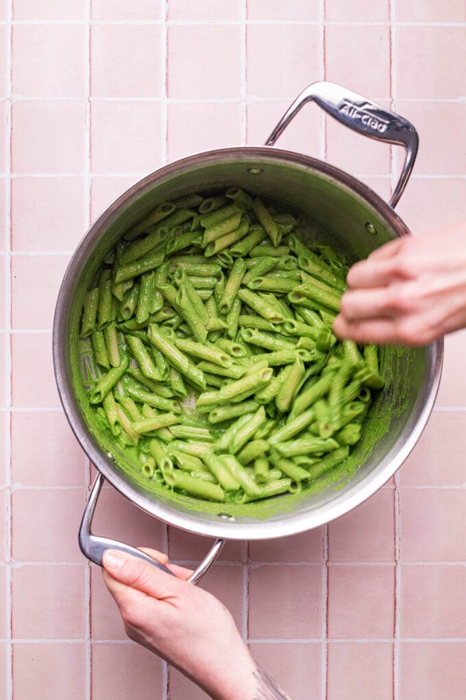 hand stirring green pasta in pot